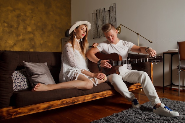 Increíble pareja joven con guitarra en el interior de la habitación. Linda mujer y hombre en el sofá con guitarra