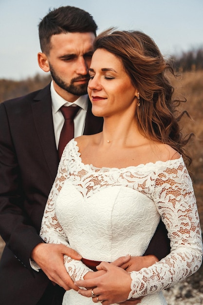 Increíble pareja de novios la novia y el novio tomados de la mano en un fondo de montañas y ríos