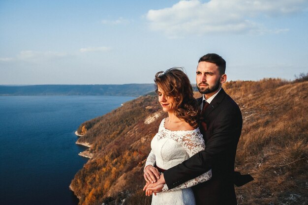 Increíble pareja de novios la novia y el novio tomados de la mano en un fondo de montañas y ríos