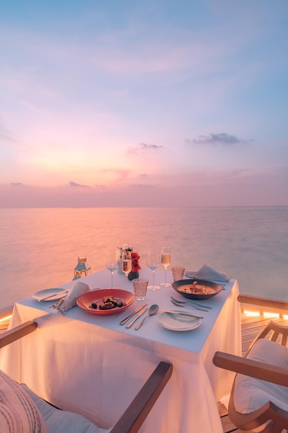 Increíble pareja romántica cena en la playa en una terraza de madera con velas bajo el cielo del atardecer. romanticismo y amor