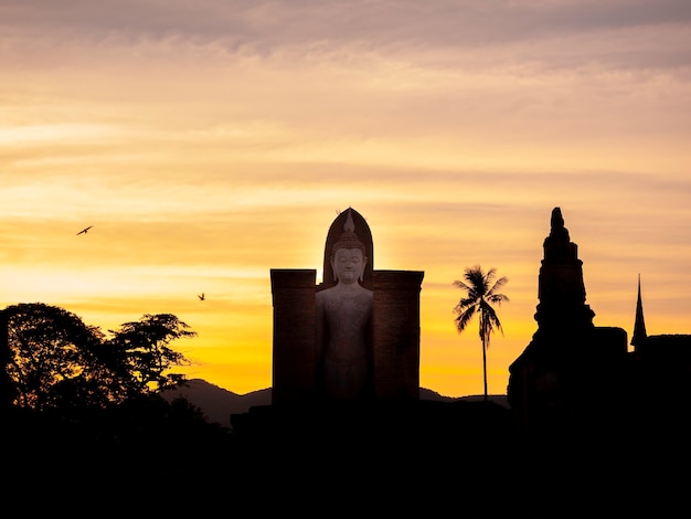 Increíble scenetic de silueta del templo Wat Mahathat en el recinto del Parque Histórico de Sukhothai con gran estatua de Buda sobre fondo de cielo dorado al atardecer, Patrimonio de la Humanidad por la UNESCO en Tailandia.