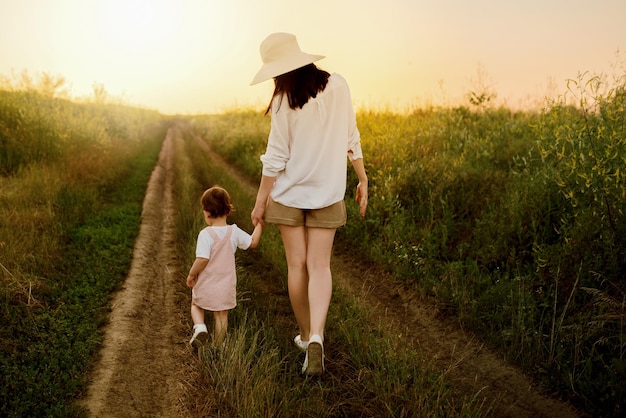 Incrível encantadora vista adorável de uma linda mãe de chapéu e filha linda andando em um caminho de um campo Pôr do sol ou nascer do sol Maternidade e infância