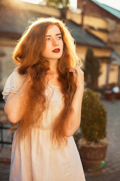 Incrível jovem ruiva com cabelo comprido e ondulado nu posando no brilho do sol ao pôr do sol