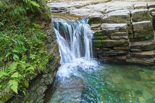 Incrível paisagem de bela cachoeira no rio de montanha com água espumosa branca caindo do penhasco rochoso na floresta tropical de verão.