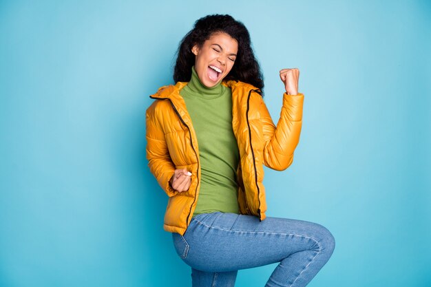 incrível pele escura e cacheada senhora comemorando jogo de futebol gritando usando casaco de primavera amarelo na moda jeans verde pulôver isolado parede azul