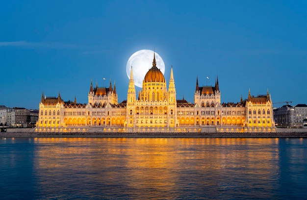 Incrível vista noturna para o edifício do parlamento húngaro e rio Danúbio com lua cheia sobre a cidade