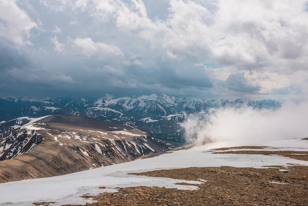 Incrível vista superior através das nuvens para altas montanhas nevadas Paisagem cênica com belas montanhas de neve em nuvens baixas Vista atmosférica alpina de colina de pedra a cordilheira de neve com nuvens baixas