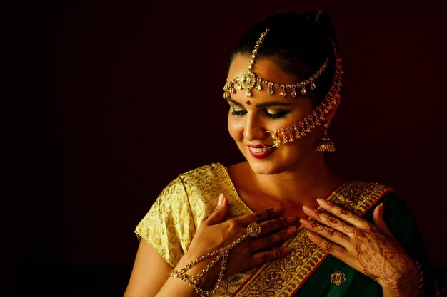 India hermosa moda mujer morena en sari rico de boda tradicional verde con joyas de oro set maquillaje profesional sobre fondo negro oscuro