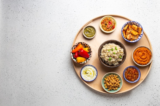 Indian thali - seleção de vários pratos servidos em travessa redonda de madeira. variedade de meze vegetariano indiano com arroz basmati cozido, paneer, dal, chutney em diferentes tigelas. vista superior, espaço para texto