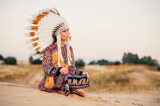 Indianerin, die in Yoga-Haltung sitzt. Kopfschmuck aus Federn von Wildvögeln. Cherokee, Navajo-Kultur, Traditionen ethnischer Völker