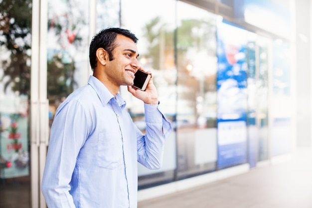 Indiano feliz falando ao telefone fora do escritório