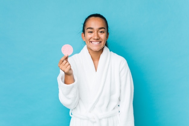 Indiano novo da raça misturada que mantém uma esponja facial feliz, sorridente e alegre.