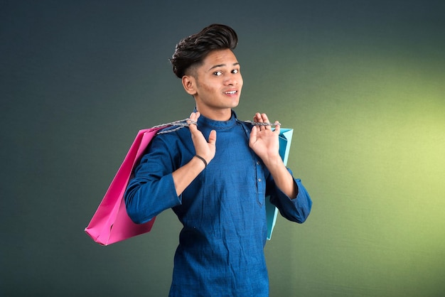 Foto indiano tradicional jovem homem bonito segurando e posando com sacos de compras em um fundo escuro