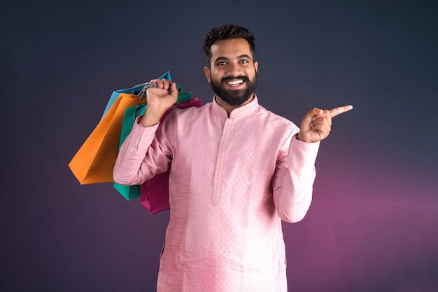 Foto indiano tradicional jovem homem bonito segurando e posando com sacos de compras em um fundo escuro