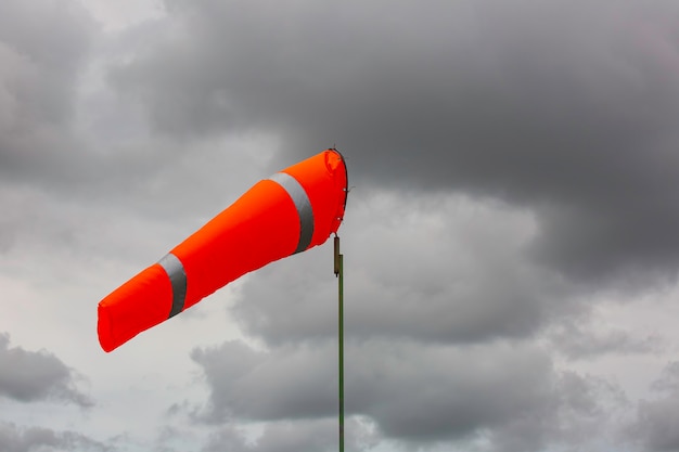 Indicador de manga de viento del viento en el cono químico del tanque que indica la dirección y fuerza del viento. Manga de viento que vuela horizontalmente (veleta) con cielo de nubes en el fondo.