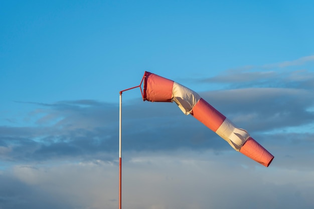 Foto indicador de viento rojo y blanco en forma de cono en el aeródromo. puesta de sol y nubes al fondo