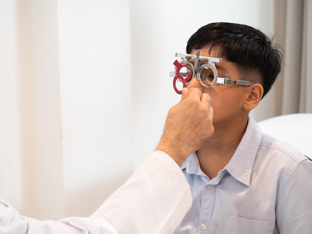 Indien süßer Junge sitzt in einem Brillengeschäft mit einem Optiker, der auf Augenerkrankungen und primäre Augengesundheit spezialisiert ist, auf der Suche nach einer Linse, die zu seinem Sehvermögen passt und die effektivste Brille erhältxA