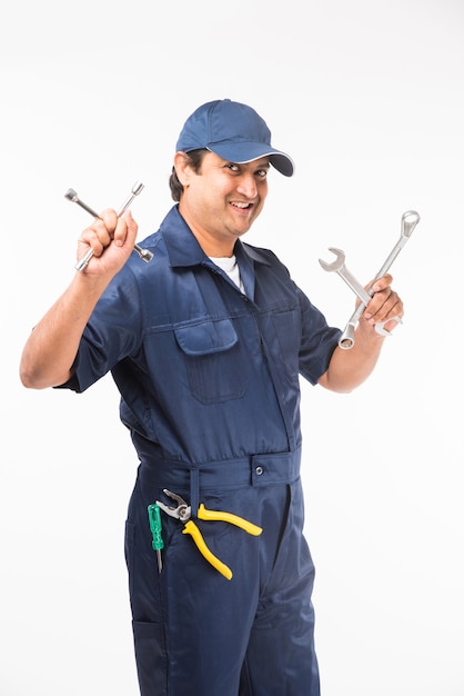 Indio feliz mecánico de automóviles en traje azul y gorra sosteniendo herramienta de llave