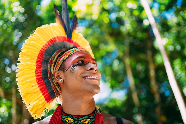 Indio de la tribu Pataxó con tocado de plumas mirando hacia la derecha. Indígena de Brasil con pinturas faciales tradicionales