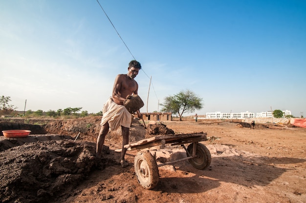 Indische Arbeiter, die Ton in der Ziegelfabrik verarbeiten und tragen