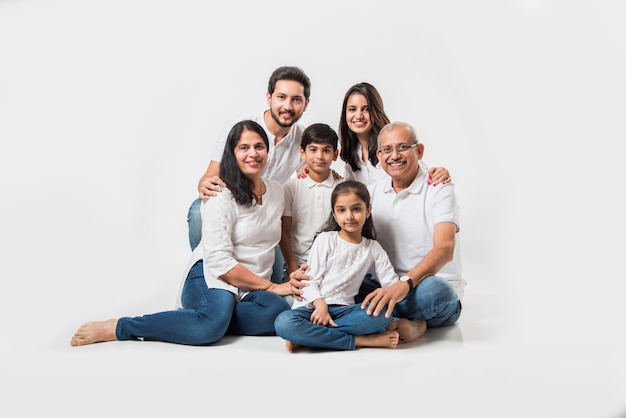 Indische asiatische Familie, die über weißem Hintergrund sitzt. älteres und junges Paar mit Kindern, die weißes Top und blaue Jeans tragen. selektiver Fokus