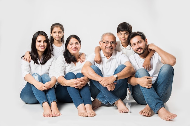 Indische asiatische Familie, die über weißem Hintergrund sitzt. älteres und junges Paar mit Kindern, die weißes Top und blaue Jeans tragen. selektiver Fokus