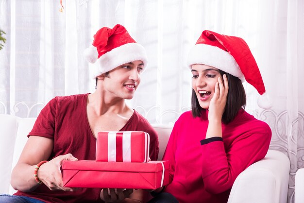 Indische asiatische junge Familie, die Weihnachten mit Geschenk feiert, während sie Weihnachtsmütze trägt