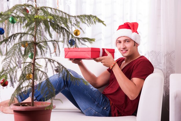 Indische asiatische junge Familie, die Weihnachten mit Geschenk feiert, während sie Weihnachtsmütze trägt