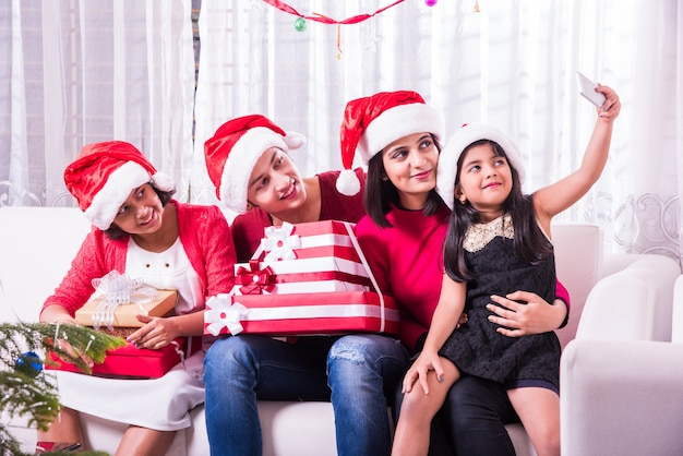 Indische asiatische junge Familie, die Weihnachten mit Geschenk feiert, während sie Weihnachtsmütze trägt