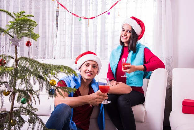 Indische asiatische junge Familie, die Weihnachten mit Geschenk feiert, während sie Weihnachtsmütze trägt