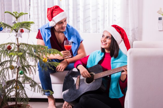 Indische asiatische junge Familie, die Weihnachten mit Geschenk feiert, während sie Weihnachtsmütze trägt