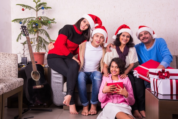 Indische asiatische junge Familie, die Weihnachten mit Geschenk feiert, während sie Weihnachtsmütze trägt