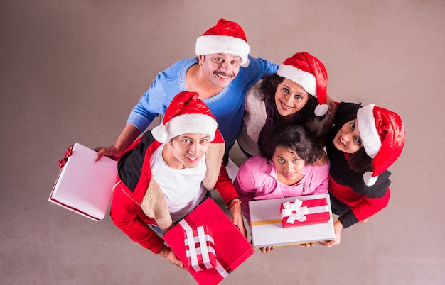 Indische asiatische junge Familie, die Weihnachten mit Geschenk feiert, während sie Weihnachtsmütze trägt