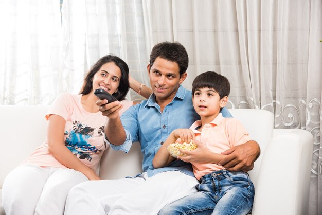 Indische asiatische junge Familie, die zusammen Fernsehen schaut, während sie auf dem Sofa sitzt, selektiver Fokus