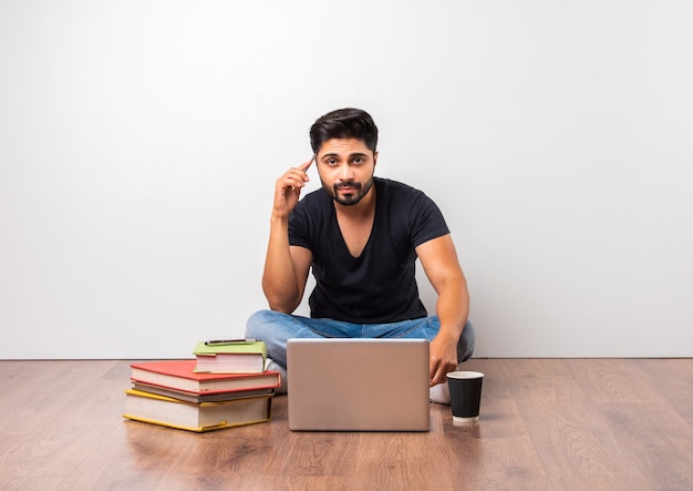 Indische asiatische Universität oder College-Student sitzt mit Laptop-Computer mit Büchern auf Holzboden vor weißem Hintergrund