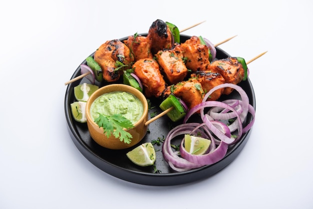 Indische Chicken Tikka Kebabs, mariniert in Gewürzen und Joghurt und im Tandoor gebraten. serviert mit grünem Chutney und Zwiebeln. selektiver Fokus