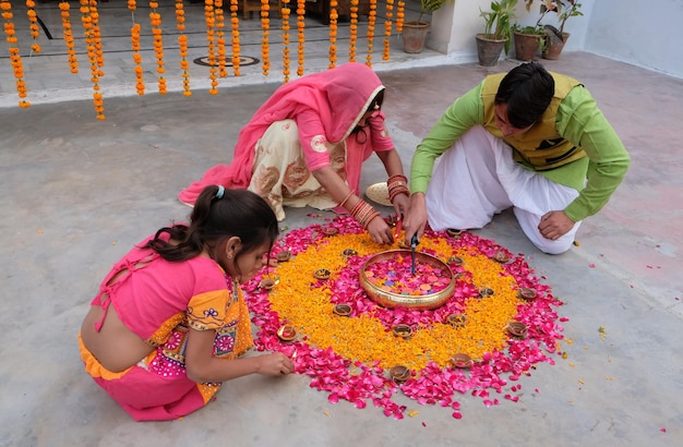 Indische Familie, die aus Kerzen, Ringelblumen und rosa Rosenblättern Rangoli auf dem Boden herstellt