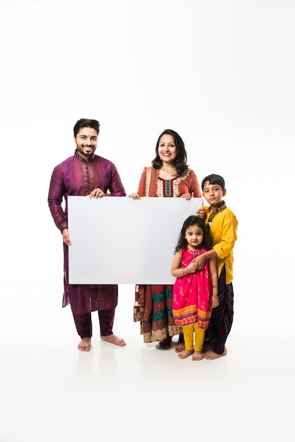 Indische Familie, die Diwali feiert, während sie ein leeres weißes Brett oder ein Plakat hält. Stehend isoliert auf weißem Hintergrund und Blick in die Kamera