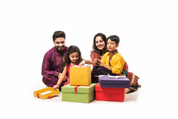 Indische Familie feiert Diwali oder Deepavali in traditioneller Kleidung beim Sitzen isoliert auf weißem Hintergrund mit Geschenkboxen und Lampe in Thali