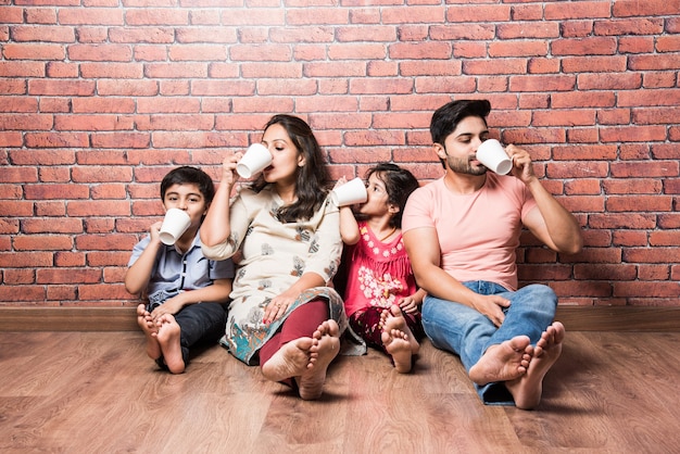 Indische Familie trinkt Milch weiß auf Holzboden gegen rote Backsteinmauer drinnen sitzen