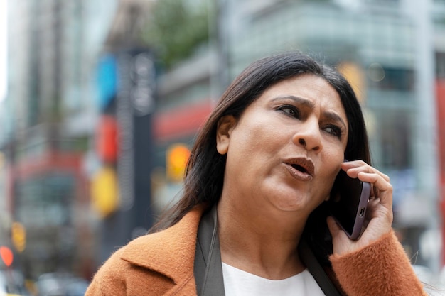 Indische Frau, die auf dem Handy spricht und auf der Straße spaziert Ernsthafte moderne weibliche Anrufbeantworter
