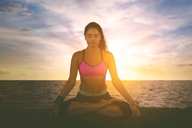 Indische Frau, die bei Sonnenaufgang Yoga an der Küste ausübt