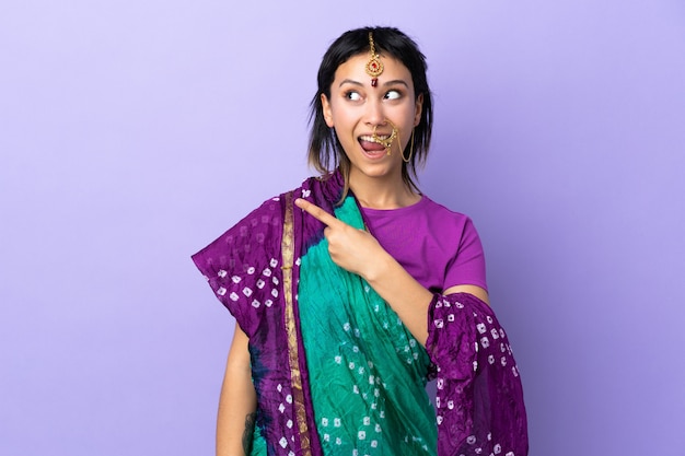 Indische Frau isoliert auf lila Wand überrascht und zeigt Seite
