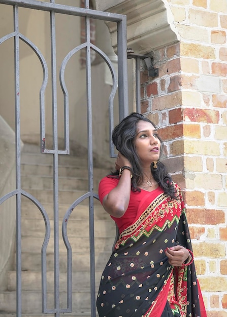Indische Frau mit rotem Saree, die vor einer Tür neben einer Ziegelmauer steht