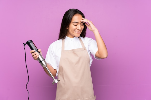 Indische Frau mit Stabmixer auf lila Wand lachen