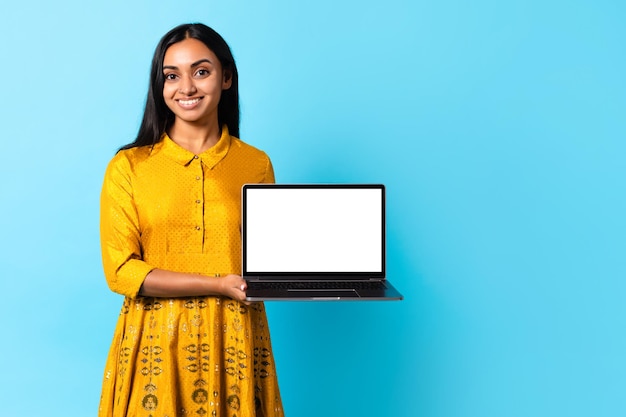 Indische Frau zeigt Laptop und posiert im traditionellen gelben Kleiderstudio
