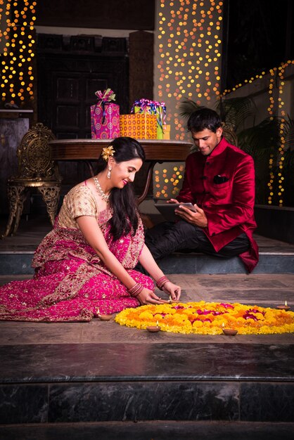 Indische junge Familie, die Blumen Rangoli macht oder Diyas für die Diwali-Festivalnacht auf der Veranda mit Geschenken und Bokeh im Hintergrund arrangiert