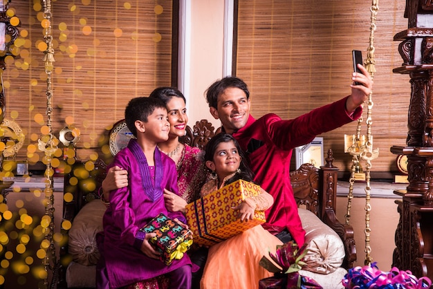 Indische junge Familie, die in der Diwali-Festivalnacht mit Geschenkboxen zu Hause Selfie oder Selbstfoto macht.