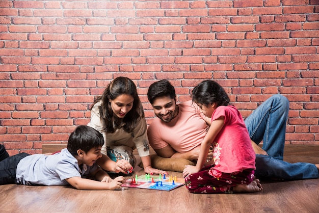 Indische junge vierköpfige Familie, die zu Hause in Quarantäne Brettspiele wie Schach, Ludo oder Snack and Ladder spielt