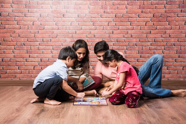 Indische junge vierköpfige Familie, die zu Hause in Quarantäne Brettspiele wie Schach, Ludo oder Snack and Ladder spielt